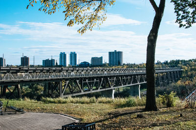 Bridge over river by buildings in city against sky