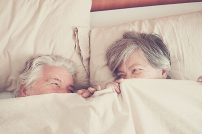 High angle view of couple hiding face by blanket while lying on bed