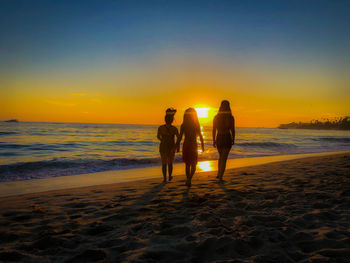 Silhouette woman walking at beach against sky during sunset
