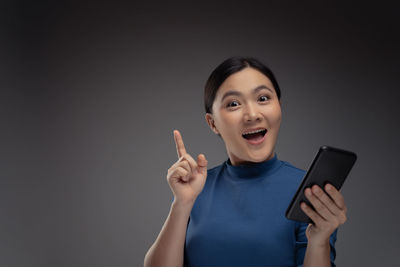 Portrait of young woman using smart phone against gray background