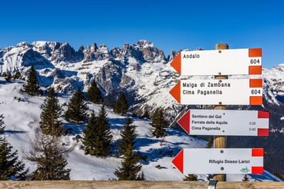 Information sign on snow covered mountain against blue sky
