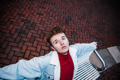 Portrait of young man sitting against brick wall