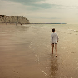 Rear view of woman walking at beach against sky
