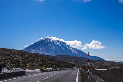 Road leading towards snowcapped mountains against blue sky