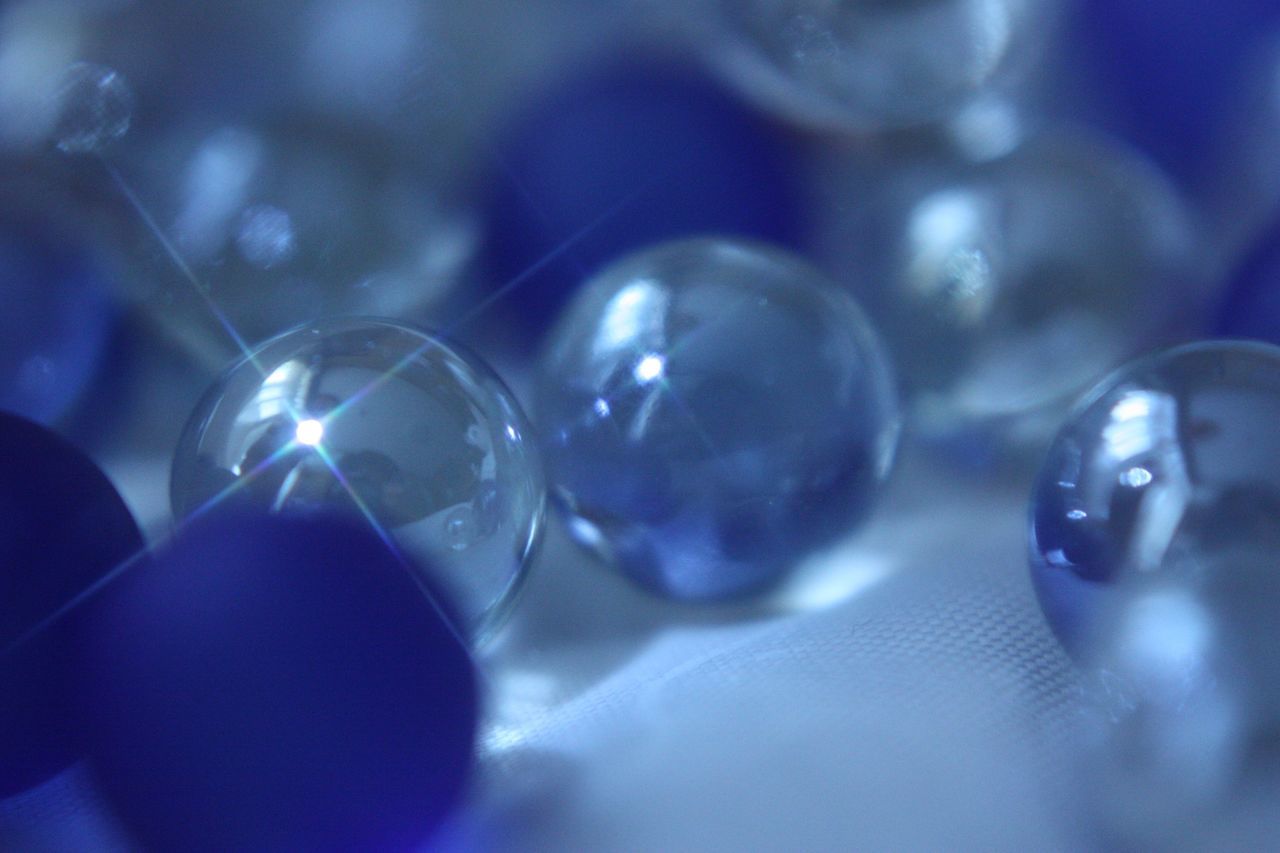 close-up, indoors, selective focus, focus on foreground, still life, reflection, shiny, sphere, transparent, glass - material, no people, bubble, large group of objects, multi colored, decoration, abundance, table, detail, fragility, blue