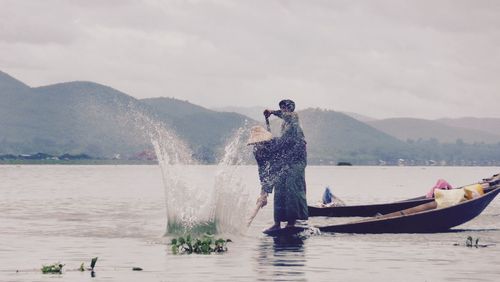 Man splashing water in river with oar against sky