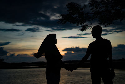 Silhouette people standing at beach against sky during sunset