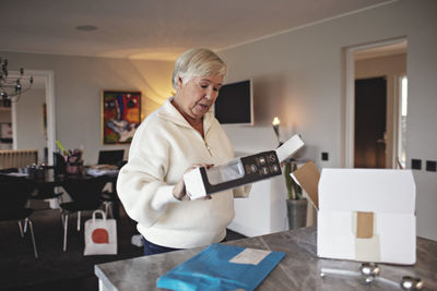 Wrinkled senior woman unpacking box over kitchen island