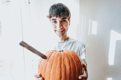 Portrait of smiling man holding pumpkin against wall
