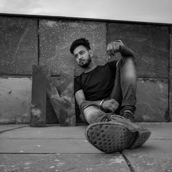 Low angle view of man sitting by wall on footpath