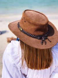Rear view of woman with long brown hair wearing hat at beach