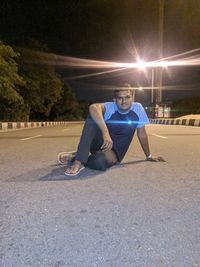 Portrait of young man sitting on road at night