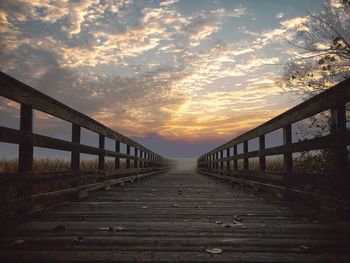 Footbridge amidst trees against sky during sunset