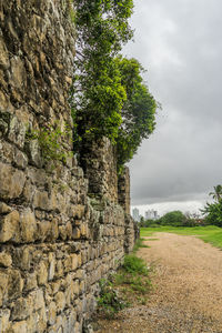 Stone wall by dirt road against sky
