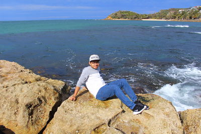 Portrait of man sitting on rock by sea against sky