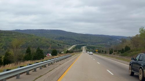 Road leading towards mountains against cloudy sky