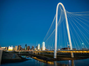 Illuminated suspension bridge over river against blue sky