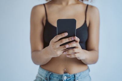 Midsection of woman holding smart phone against gray background