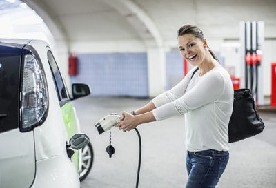 Side view portrait of playful woman electrical charger pump at gas station