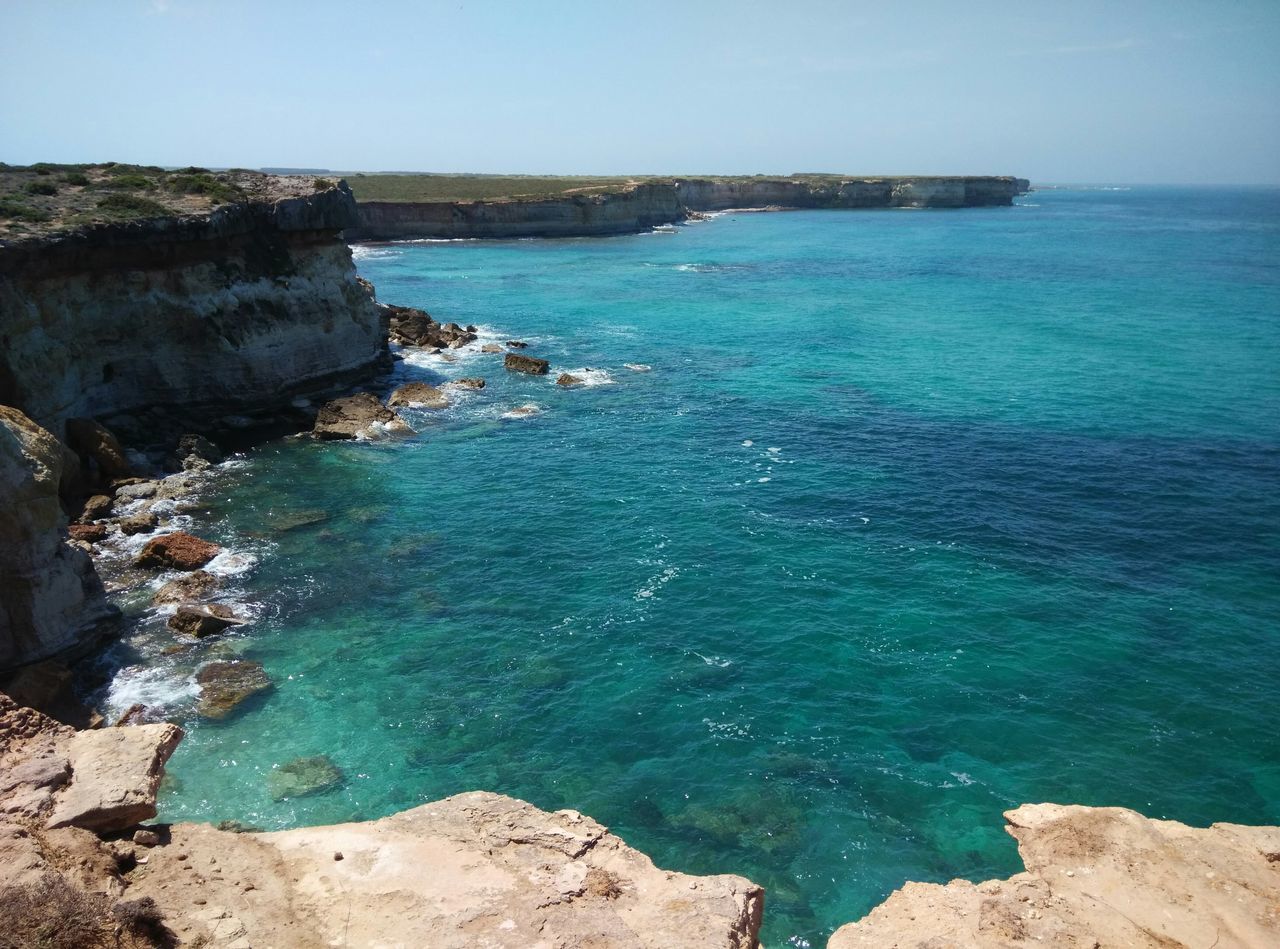 water, sea, blue, tranquil scene, tranquility, scenics, beauty in nature, rock - object, horizon over water, nature, clear sky, rock formation, rock, rippled, idyllic, cliff, high angle view, day, seascape, outdoors