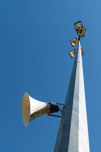 Low angle view of sports field tower with a bullhorn speaker and floodlights against clear blue sky