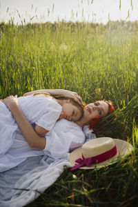 Girl a child hug mother woman with red hair lying on a green field at sunset