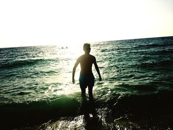 Rear view of silhouette boy standing on beach against clear sky