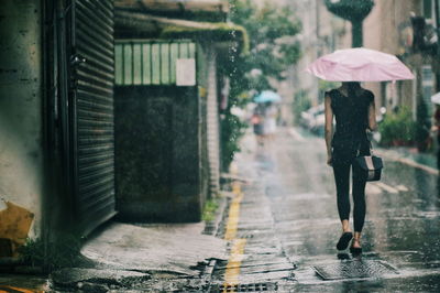 Rear view of woman with umbrella walking on footpath in rain