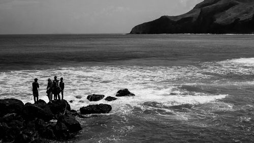 People standing on rocks by sea against sky