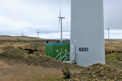 Close-up view of wind turbine base in field against sky