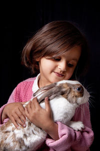 Close-up portrait of young woman holding animal over black background