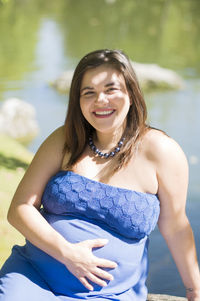 Portrait of a happy pregnant woman in a bright blue dress and sitting on a bench