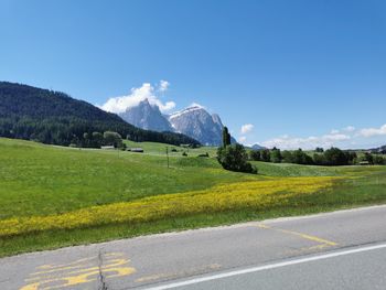 Scenic view of road amidst field against blue sky