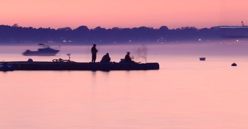 Silhouette people on lake against sky during sunset
