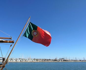 Low angle view of portuguese flag over sea against clear blue sky