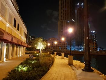 Illuminated street amidst buildings against sky at night