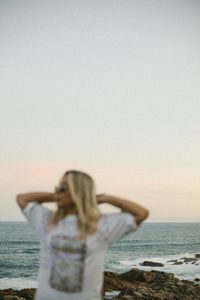 Rear view of woman standing at beach against sky