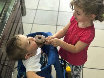 High angle view of sister feeding donut to brother while standing on floor