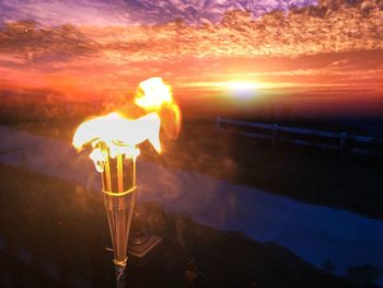 Close-up of illuminated candle against sky at sunset