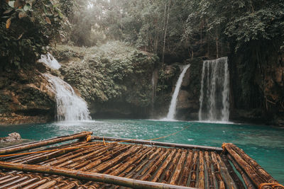 Wooden raft on river against waterfall at forest