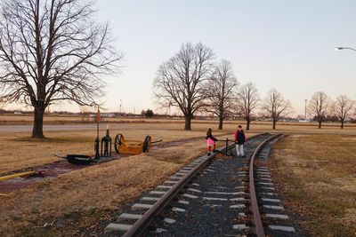 Siblings on railroad track against sky during sunset