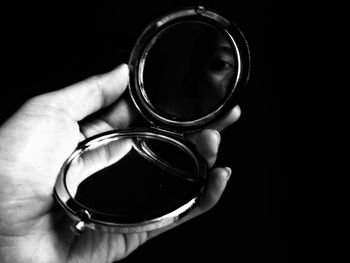 Cropped hand of woman holding mirror against black background