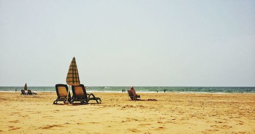 People sitting on beach against clear sky