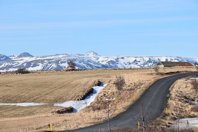 Road by snowcapped mountains against blue sky