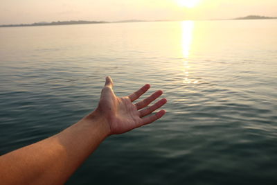 Close-up of human hand against lake during sunset