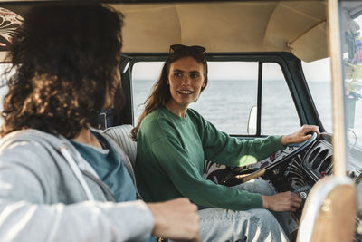 Woman talking with male friend while sitting in van by sea