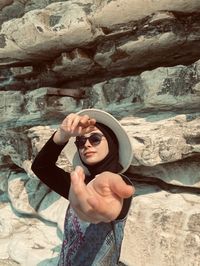 Young woman wearing sunglasses standing against rock formation