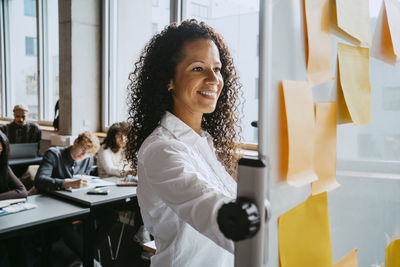 Smiling teacher looking at whiteboard while teaching students in classroom