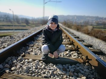 Portrait of cute boy crouching on railroad track