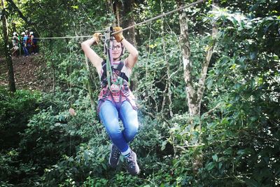 Full length of woman on zip line against trees at forest